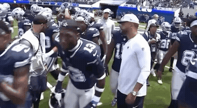 A Group Of Football Players Are Walking On A Field With Their Coach . GIF