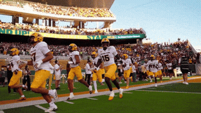 A Group Of Football Players Running On A Field With A Sign That Says No Up GIF