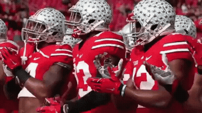 A Group Of Football Players Wearing Red Jerseys And Helmets Are Standing In A Line . GIF