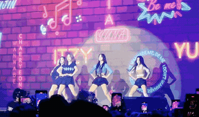 A Group Of Girls Are Performing In Front Of A Neon Sign That Says Wannabe GIF