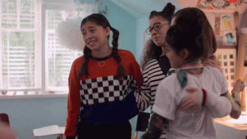 A Group Of Girls Are Standing In A Room And One Girl Is Wearing A Checkered Sweater GIF