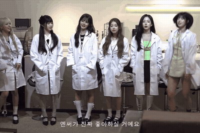 A Group Of Girls In Lab Coats Are Standing In A Line GIF