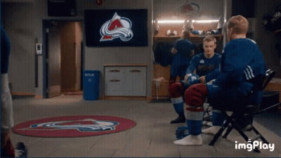 A Group Of Hockey Players Are Sitting In A Locker Room With A Tv Screen Behind Them That Says Avalanche On It GIF