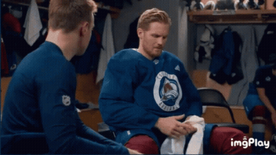 A Group Of Hockey Players Are Sitting In A Locker Room With The Colorado Avalanche Logo On A Wall GIF