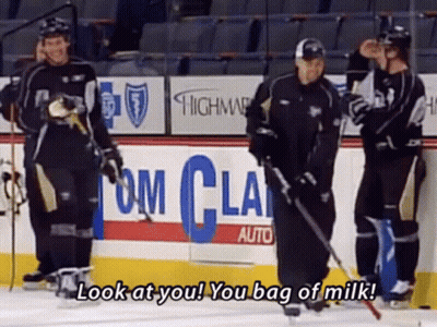 A Group Of Hockey Players Are Standing On A Rink With A Sign That Says Look At You You Bag Of Milk GIF