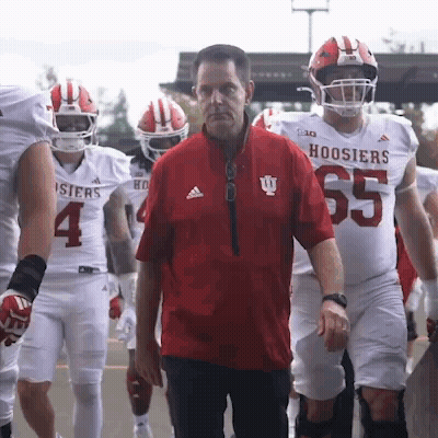 A Group Of Hoosier Football Players Are Walking Towards A Man In A Red Jacket GIF