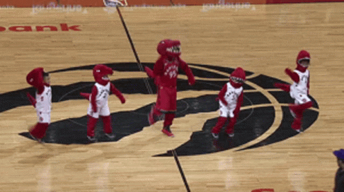 A Group Of Kids Dressed As Raptors Mascots Are Dancing On The Court GIF