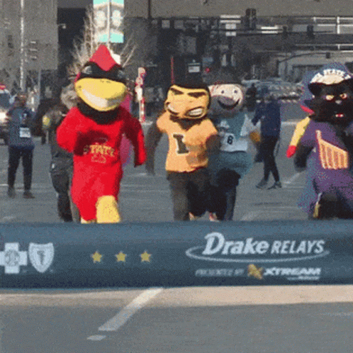 A Group Of Mascots Are Running Past A Drake Relays Sign GIF