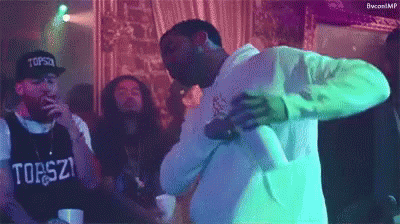 A Group Of Men Are Dancing In A Room With A Man Wearing A Shirt That Says ' Tops ' On It . GIF