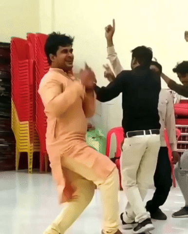 A Group Of Men Are Dancing In A Room With Stacks Of Chairs In The Background GIF