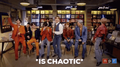 A Group Of Men Are Dancing In A Room With The Words " Is Chaotic " Above Them GIF