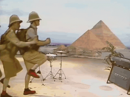 A Group Of Men Are Dancing In Front Of A Pyramid In The Desert GIF