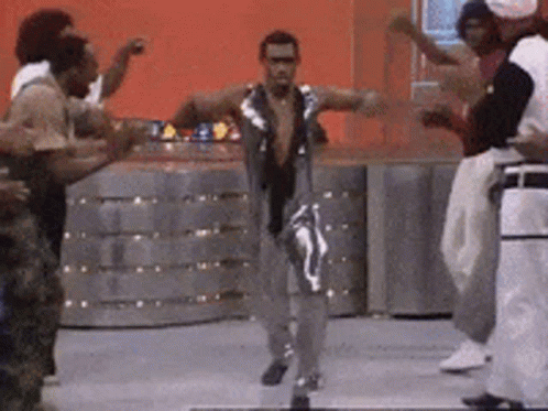 A Group Of Men Are Dancing In Front Of A Red Wall GIF