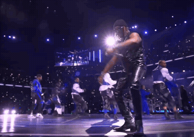 A Group Of Men Are Dancing On A Stage In Front Of A Large Screen GIF