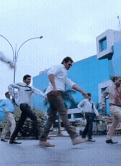 A Group Of Men Are Dancing On A Street In Front Of A Building . GIF