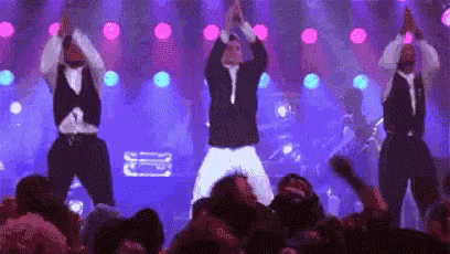 A Group Of Men Are Dancing On Stage In Front Of A Crowd . GIF