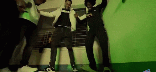 A Group Of Men Are Dancing Together In A Room With A Green Background . GIF
