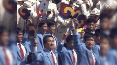 A Group Of Men Are Holding Up Their Fans In Front Of The Olympics Logo GIF