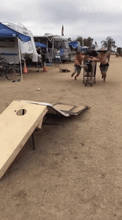 A Group Of Men Are Playing A Game Of Cornhole On A Sandy Field GIF