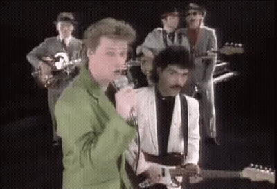 A Group Of Men Are Playing Guitars And Singing Into Microphones While Standing Next To Each Other On A Stage . GIF