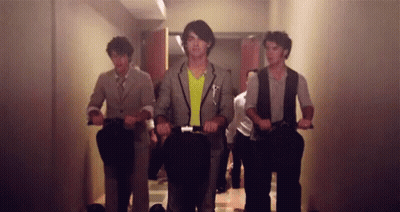 A Group Of Men Are Riding Scooters In A Hallway GIF