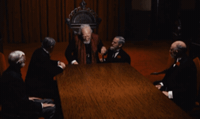A Group Of Men Are Sitting Around A Table With A Man Standing In The Middle GIF