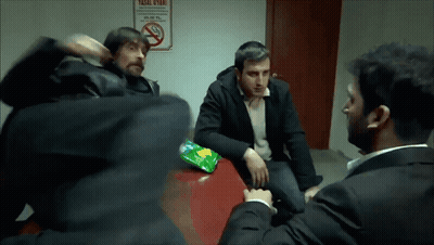 A Group Of Men Are Sitting Around A Table With A No Smoking Sign Behind Them GIF