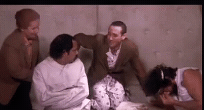 A Group Of Men Are Sitting Around A Woman In A Strait Jacket . GIF