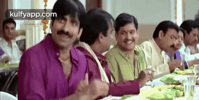 A Group Of Men Are Sitting At A Long Table Eating Food . GIF