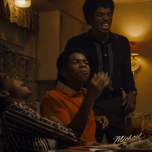 A Group Of Men Are Sitting At A Table With A Sign That Says Michael On It GIF