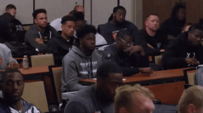 A Group Of Men Are Sitting In A Classroom With One Wearing A Hoodie That Says Buckeyes GIF