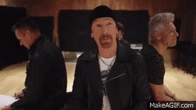 A Group Of Men Are Sitting In A Room And One Of Them Has A Beard And A Black Jacket On . GIF