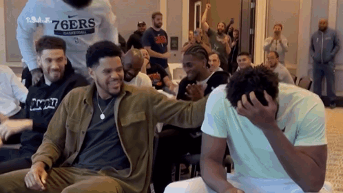 A Group Of Men Are Sitting In A Room Laughing And One Man Is Covering His Face . GIF