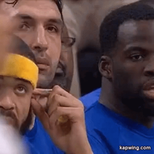 A Group Of Men Are Sitting In A Stadium Watching A Game . One Of The Men Is Wearing A Yellow Headband . GIF
