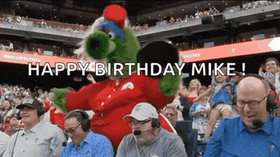 A Group Of Men Are Sitting In A Stadium With A Mascot And The Words `` Happy Birthday Mike '' . GIF