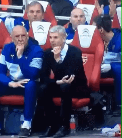 A Group Of Men Are Sitting In The Stands Of A Soccer Game . GIF
