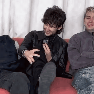 A Group Of Men Are Sitting On A Couch Laughing And Holding A Microphone . GIF