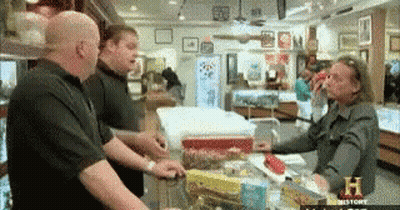 A Group Of Men Are Standing Around A Counter In A Store That Says History On The Bottom GIF