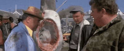 A Group Of Men Are Standing Around A Large Shark . GIF