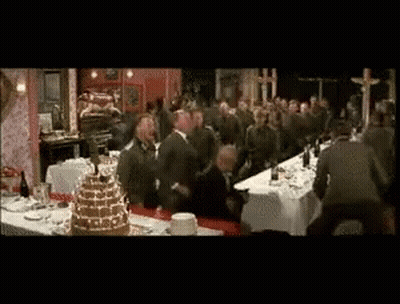 A Group Of Men Are Standing Around A Long Table With A Cake On It GIF