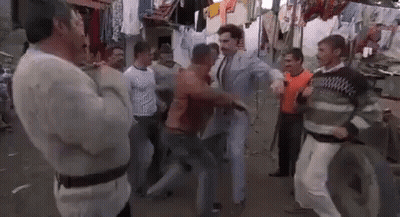 A Group Of Men Are Standing Around A Man In A Suit Dancing On A Street . GIF