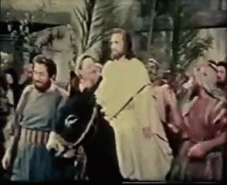 A Group Of Men Are Standing Around A Man In A White Robe Holding A Sword . GIF