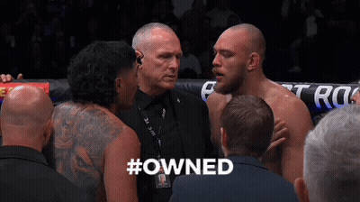A Group Of Men Are Standing In A Boxing Ring And One Of Them Has The Word #Owned On His Back GIF
