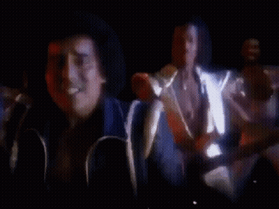 A Group Of Men Are Standing In A Dark Room Playing Guitars And Singing . GIF