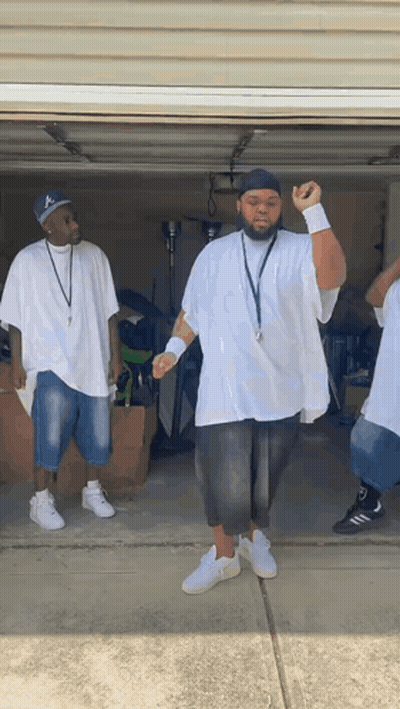 A Group Of Men Are Standing In A Garage Wearing White Shirts And Black Shorts GIF