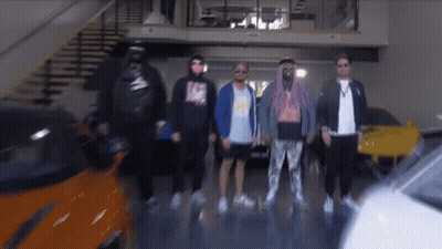 A Group Of Men Are Standing In A Garage With A Car In The Background GIF