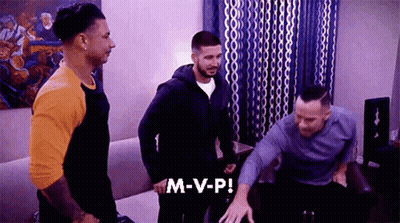A Group Of Men Are Standing In A Living Room And One Of Them Is Saying M-V-P ! GIF