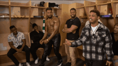 A Group Of Men Are Standing In A Locker Room And One Of Them Is Wearing A Shirtless Shirt GIF