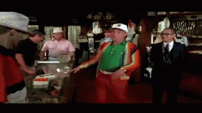 A Group Of Men Are Standing In A Room And One Of Them Is Wearing A Green Sweater GIF