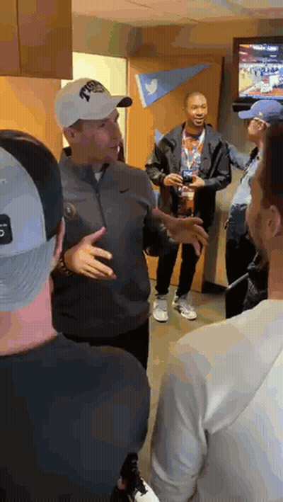 A Group Of Men Are Standing In A Room Talking To Each Other . One Of The Men Is Wearing A Nike Hat . GIF